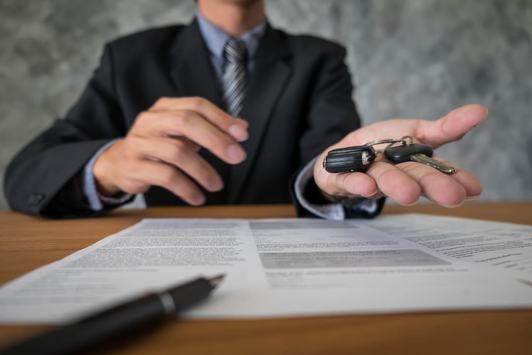 Homem entregando chave de carro sobre contrato assinado, simbolizando finalização de compra em leilão de veículos.