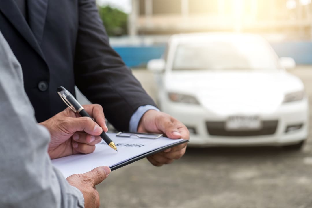 Pessoa assinando documentos com carro ao fundo, representando compra em leilão de veículos.
