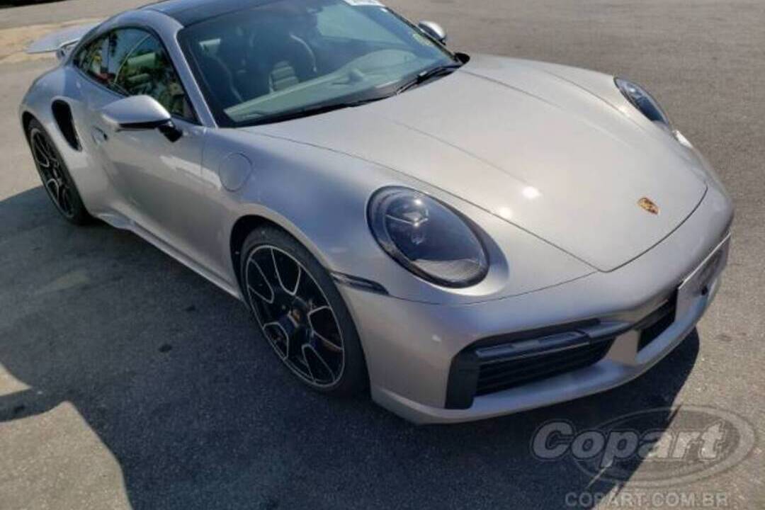 Porsche 911 Turbo S prata, carro esportivo de alto padrão, fotografado em pátio asfaltado — símbolo do mercado de luxo automotivo.