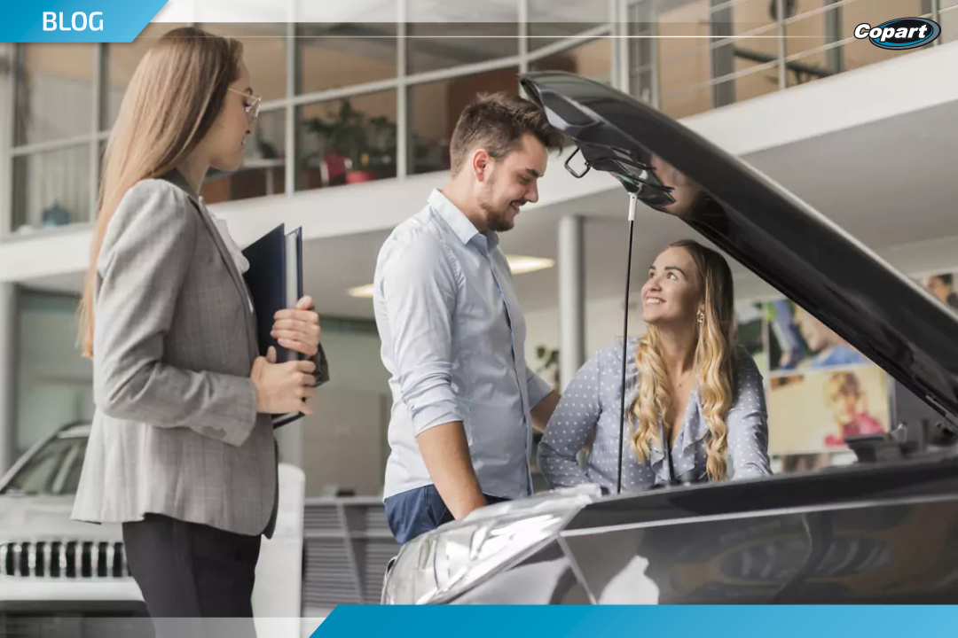 Casal avaliando motor de carro com consultora ao lado em ambiente de exposição, simbolizando compra em leilão de veículos.