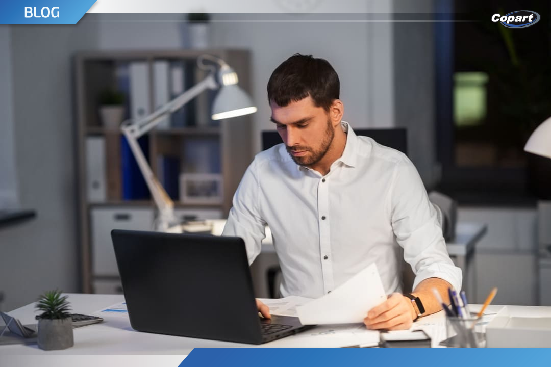 Homem analisando um laudo cautelar em frente ao notebook, em ambiente de escrit&oacute;rio &agrave; noite.
