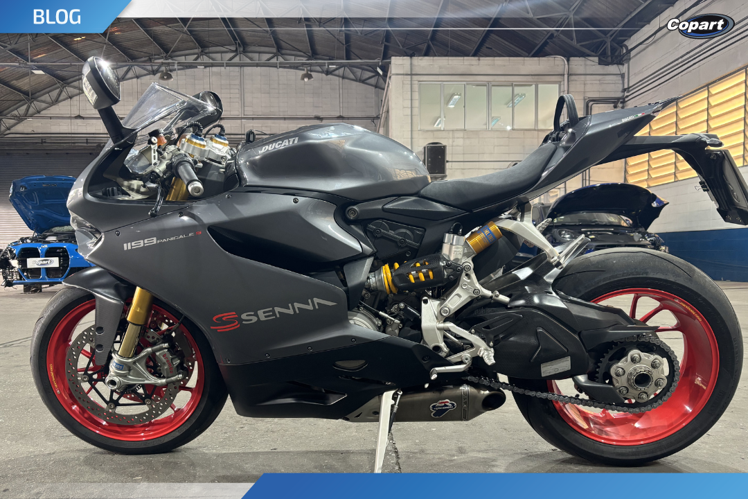 Moto esportiva cinza escuro com rodas vermelhas, exposta em ambiente fechado da empresa Copart.