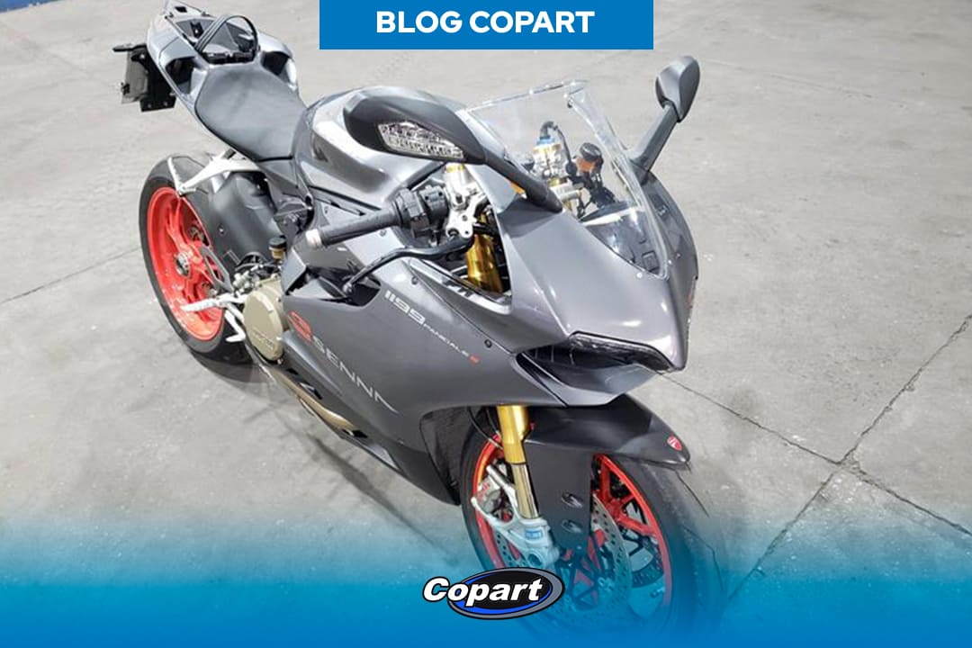 Moto esportiva cinza escuro com rodas vermelhas, exposta em ambiente fechado da empresa Copart.