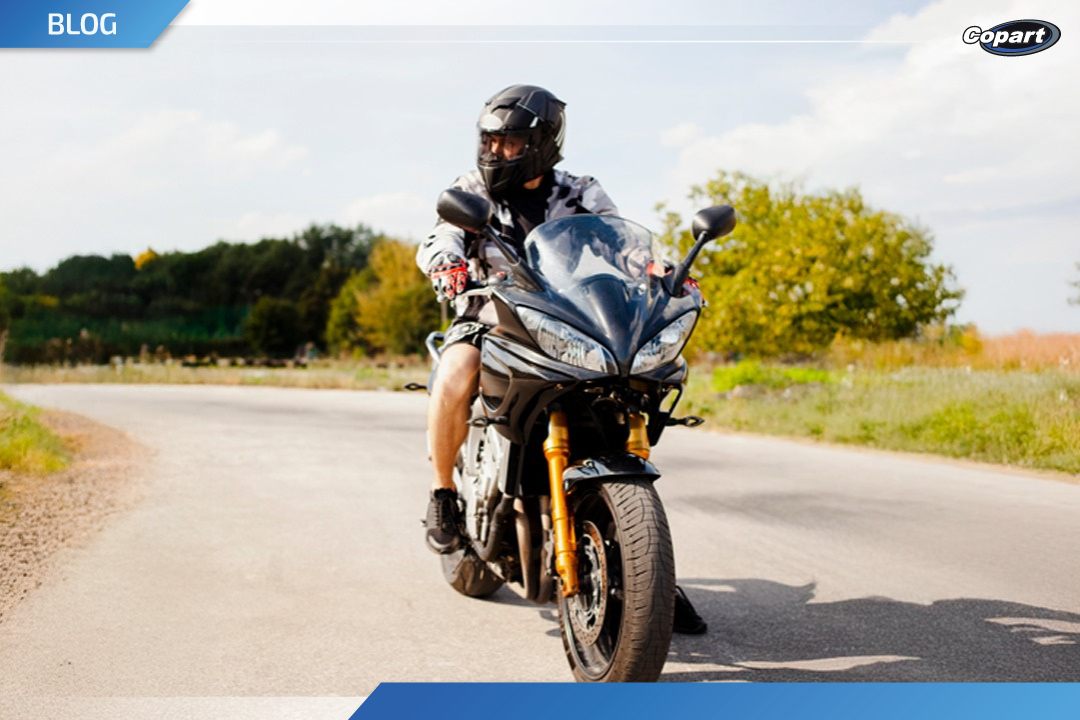 Motociclista com capacete pilotando uma moto esportiva preta em uma estrada curva ao ar livre.