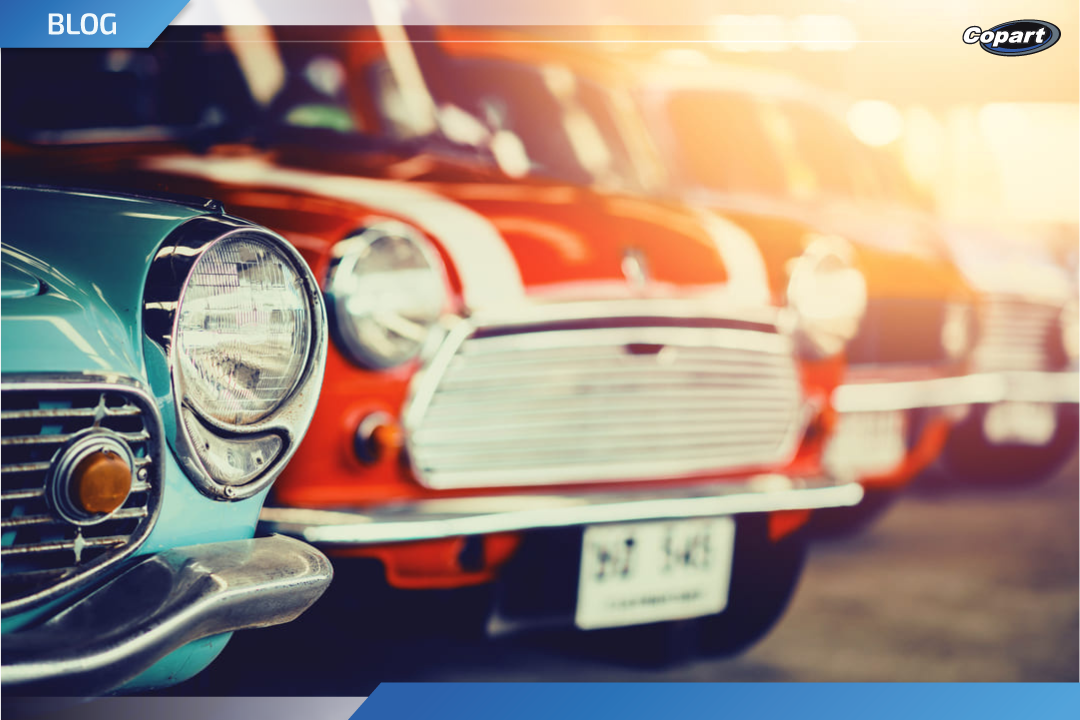 Fila de carros antigos coloridos estacionados, com destaque para os faróis e grades frontais sob luz suave do pôr do sol.