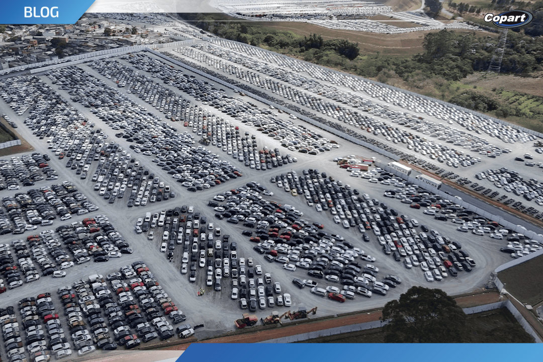 Vista aérea de um grande pátio com milhares de carros estacionados, onde muitos são classificados como veículo sinistrado aguardando leilão ou destinação.
