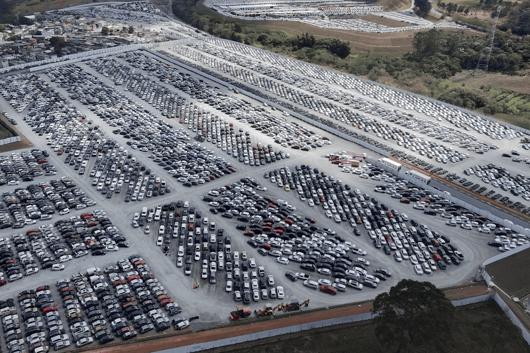 Vista aérea de um grande pátio com milhares de carros estacionados, onde muitos são classificados como veículo sinistrado aguardando leilão ou destinação.