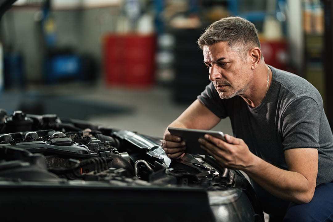Mecânico analisando o motor de um carro com auxílio de um tablet, representando o uso de inteligência artificial no mercado automotivo.