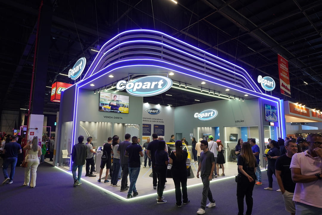 Estande da Copart no Salão do Automóvel com grande fluxo de visitantes e iluminação em LED roxo.