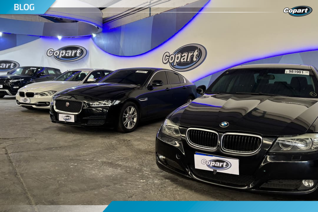 Fila de veículos premium, incluindo BMW e Jaguar, expostos em um galpão da Copart com iluminação azul, representando a Copart venda direta de veículos.