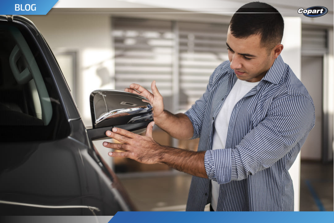 Homem analisando o retrovisor de um carro em ambiente de garagem, avaliando detalhes do veículo antes de decidir por quanto vender seu carro.