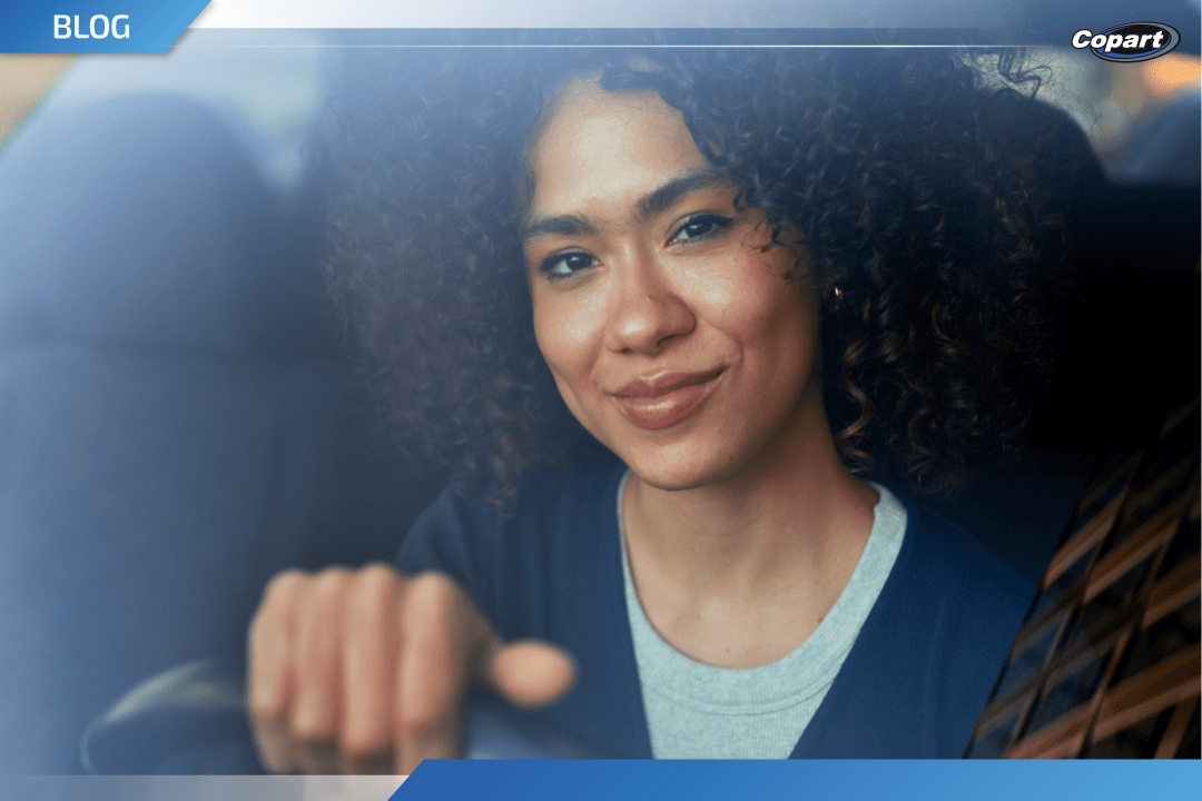 Mulher sorrindo enquanto dirige um carro, com a mão no volante. Imagem usada em banner de blog da Copart.